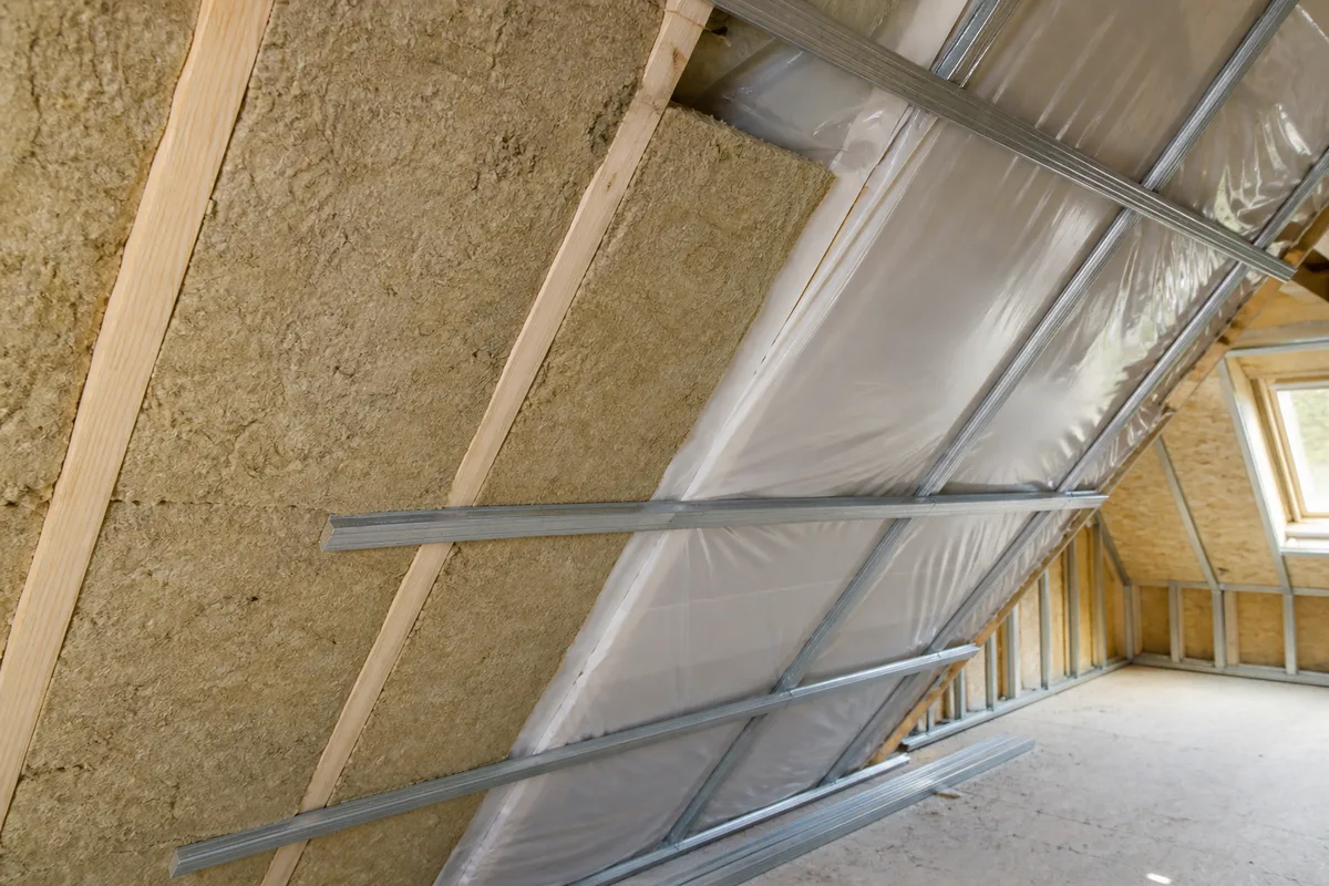 Isolant en laine posé entre chevrons dans un comble en cours de rénovation, pare-vapeur tendu, lumière naturelle latérale