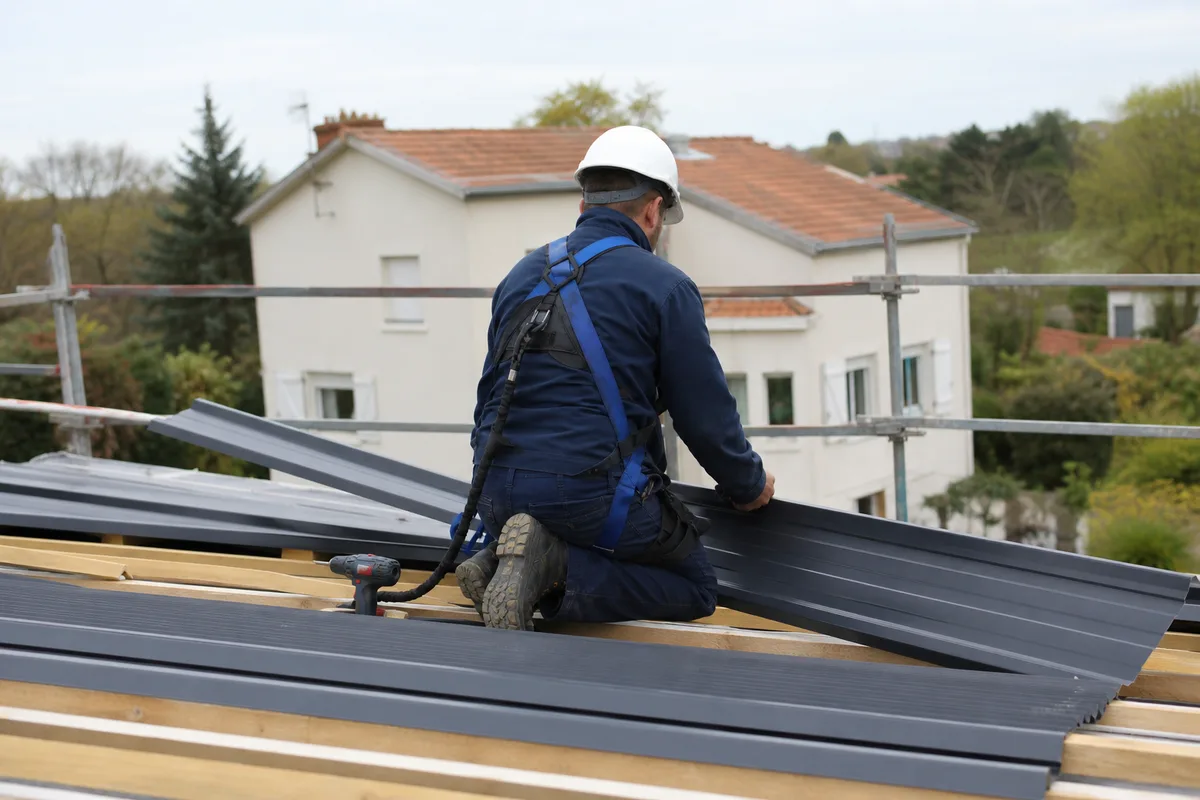 Couvreur posant des plaques de bac acier sur la charpente d&rsquo;une extension de maison