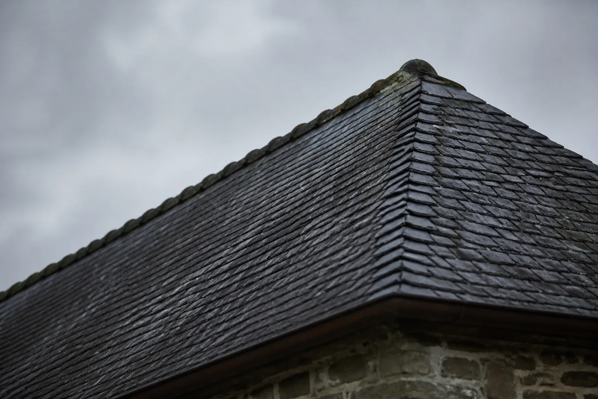 Vue en contre-plongée d&rsquo;un toit en ardoise sur ciel gris, ligne de faîtage et rampant visibles